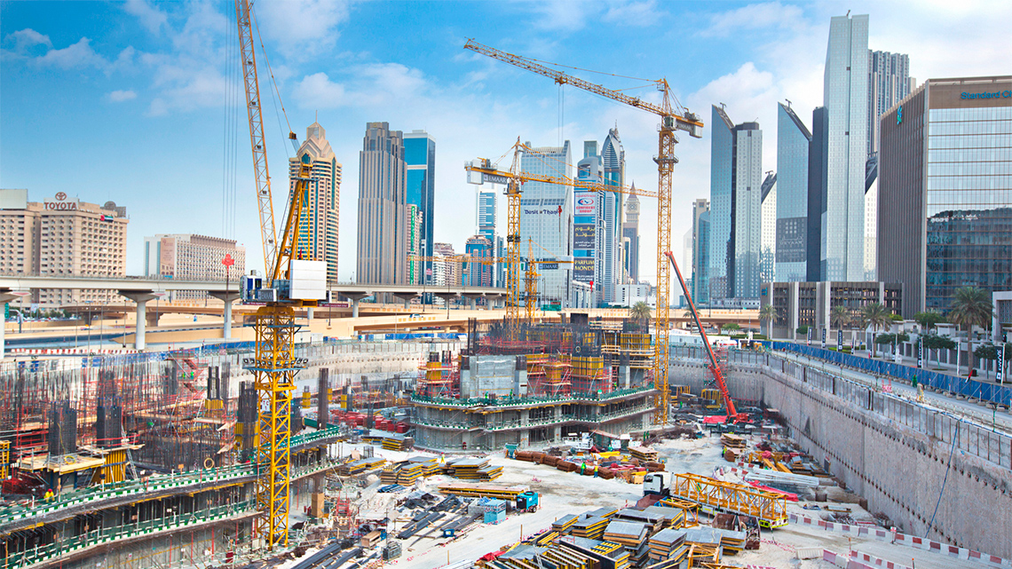 A  large construction site with cranes, high rise buildings and a highway.