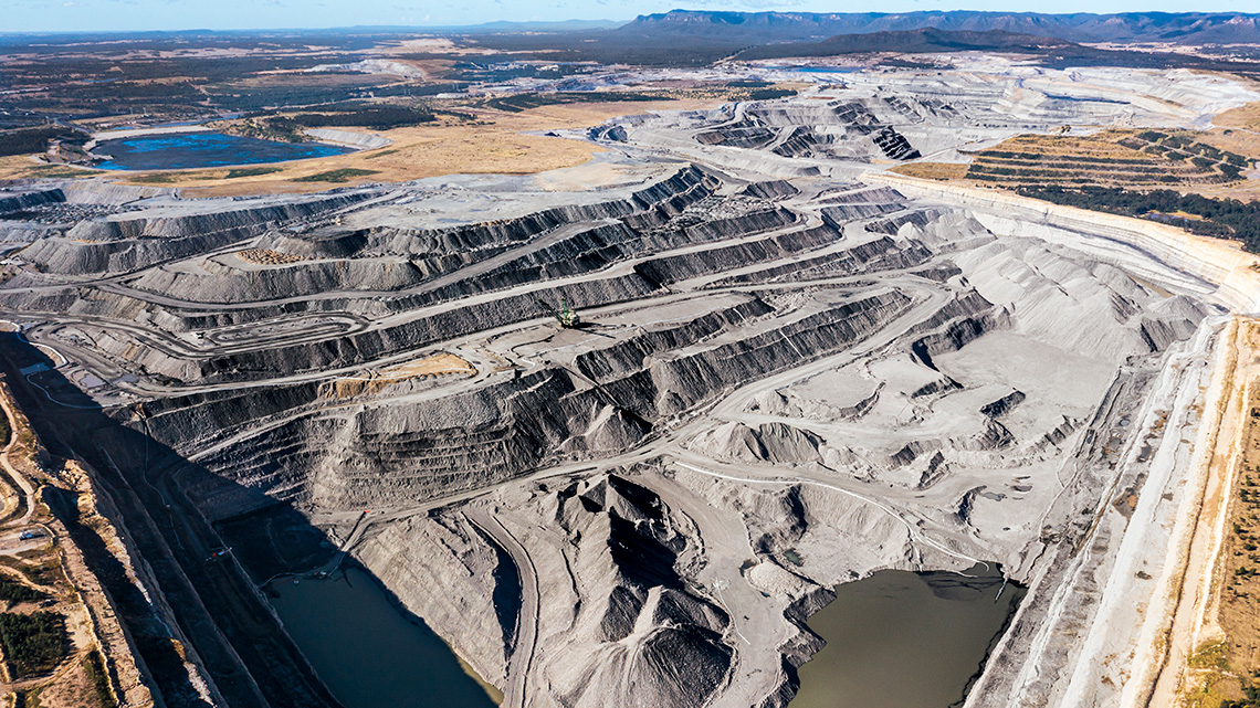 An open pit mine in India. Mine is shallow with dark soil on several different flat levels.