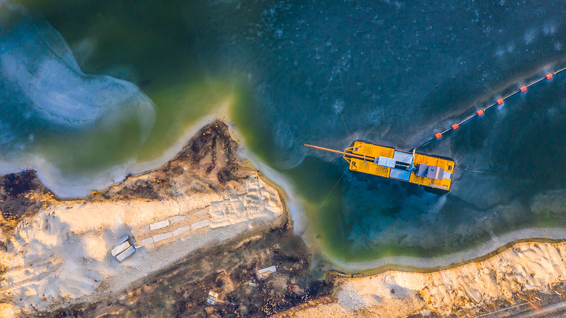 A barge travels across a lake to bring machinery to a mine located beside the lake.