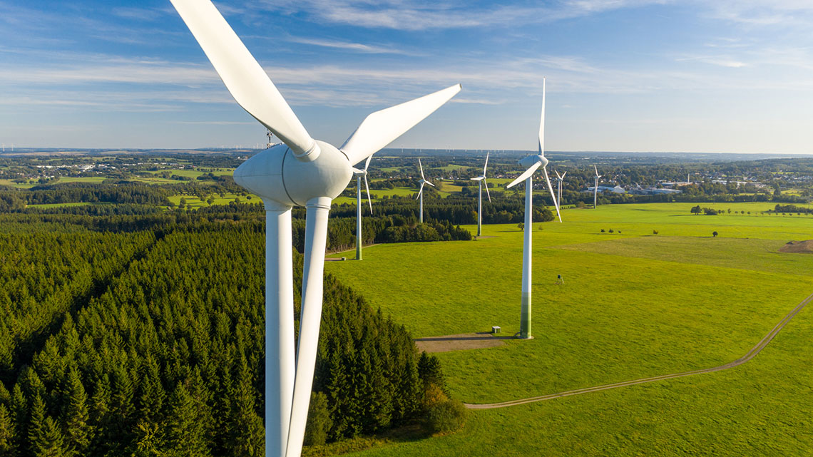 The image shows three-blade wind turbines in a field with rolling hills.
