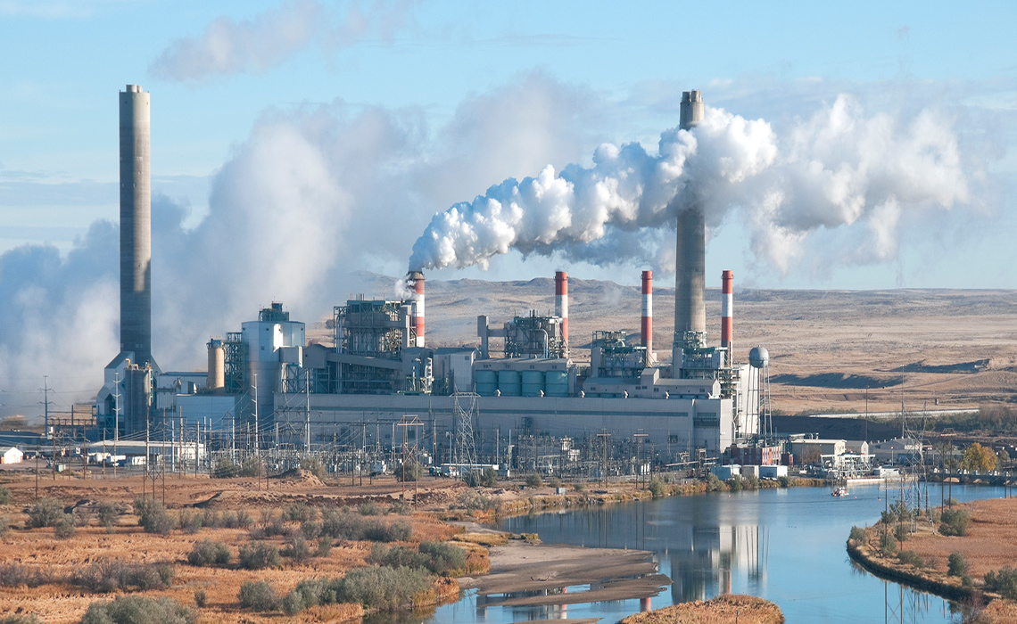 Large piles of coal sit in front of a coal refinery. Smokes rises from stacks. The air is polluted.