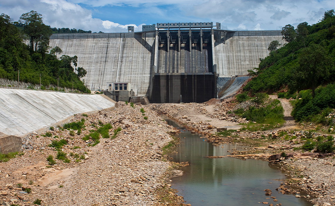 The image shows a hydroelectric power dam in Cambodia. The dam crosses the wide river.
