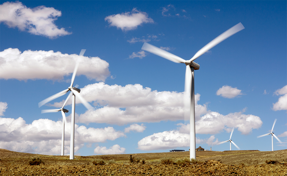 A few tall three-blade wind turbines in an otherwise empty grass field.