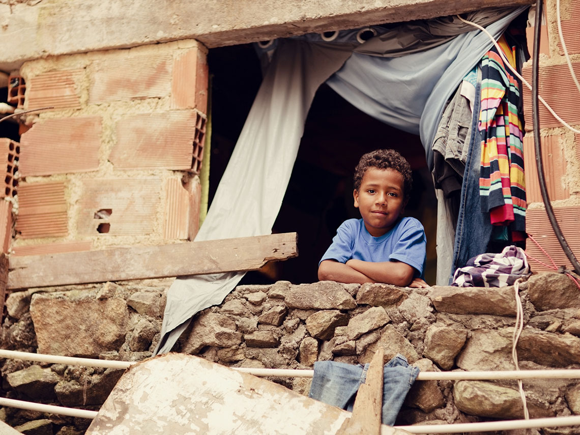 A boy staring out a window in Rio de Janeiro, Brazil. The building is brick and broken wood.