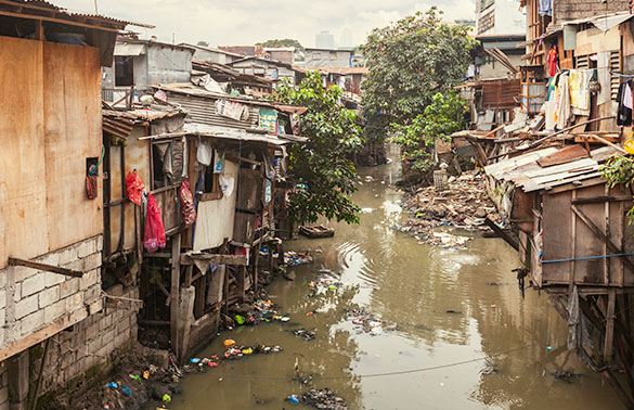 Street flooded with water and garbage. Buildings on the street are made of wood and metal scraps.