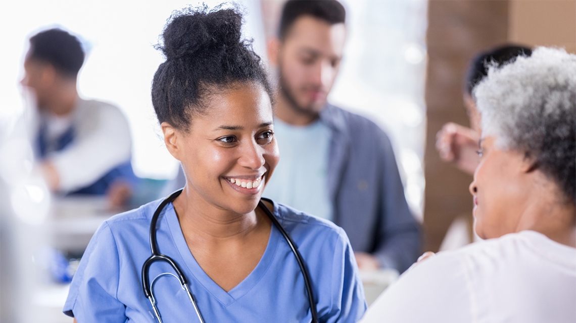 Smiling woman nurse talks with a senior woman. The nurse is volunteering in a free clinic.