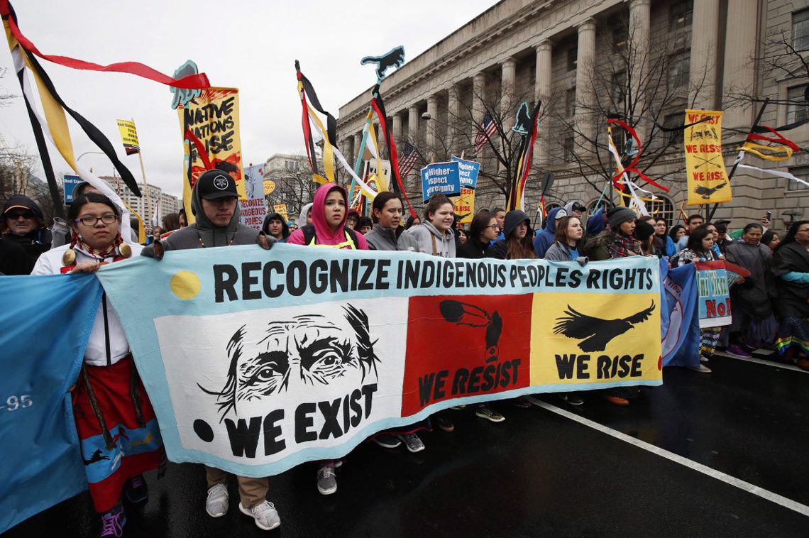 An Indigenous march with people holding a sign titled 'Recognize Indigenous Peoples Rights. We exist. We resist. We rise.'