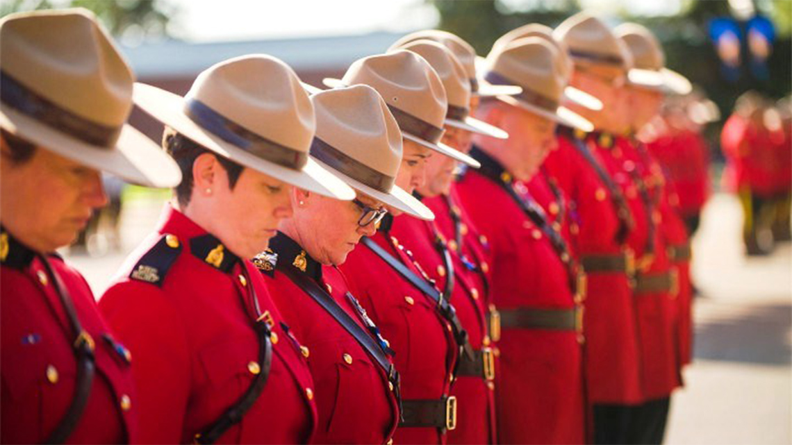 RCMP officers with red uniform and brown hats. All standing in a formed line. The officers are both male and female.