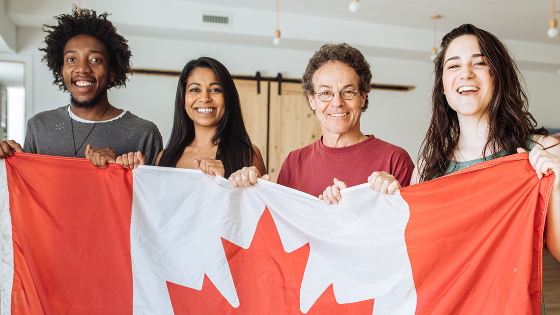 Individuals from diverse age groups and cultures holding a Canada flag together smiling.