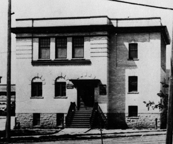 A building with ten windows. The main doors has a staircase leading to a sidewalk.