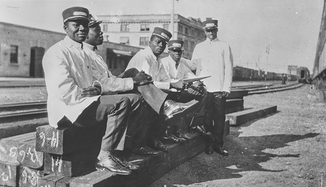 Five Black men sitting on a railway track. They are dressed in white railway uniforms.