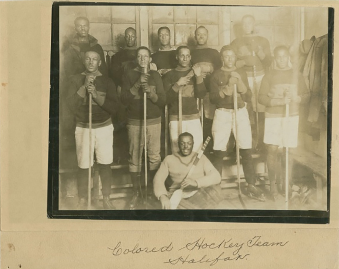 A team of Black hockey players posing for a team photo, holding hockey sticks and wearing their uniforms