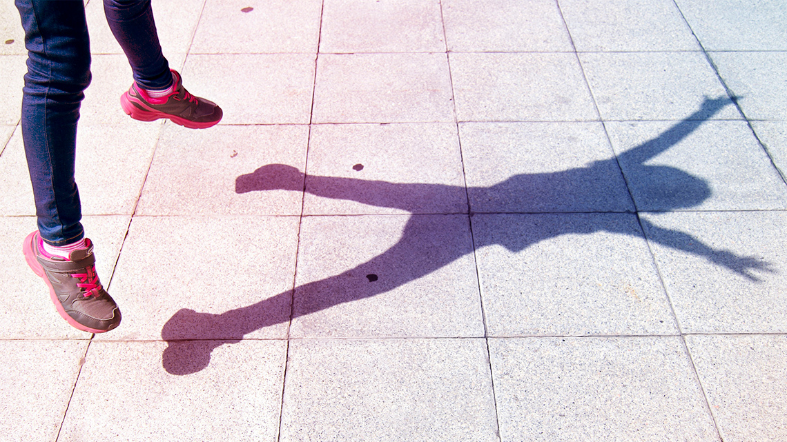 A child jump outsides with arms raised high.