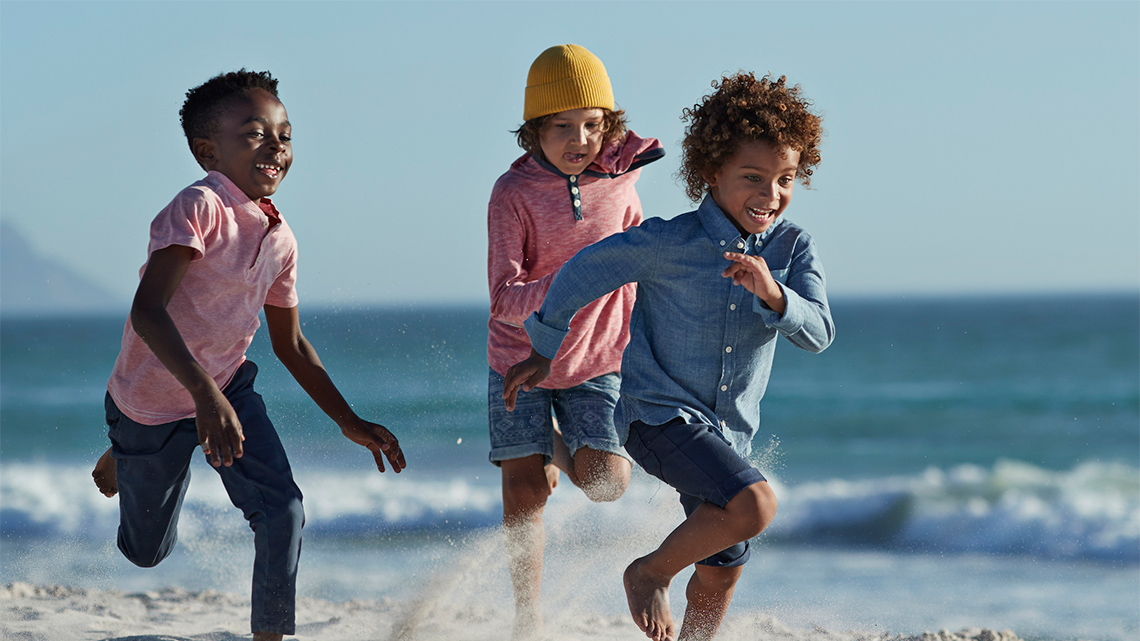 Three children are running at a beach shore line. Two are smiling and one is focused on running.