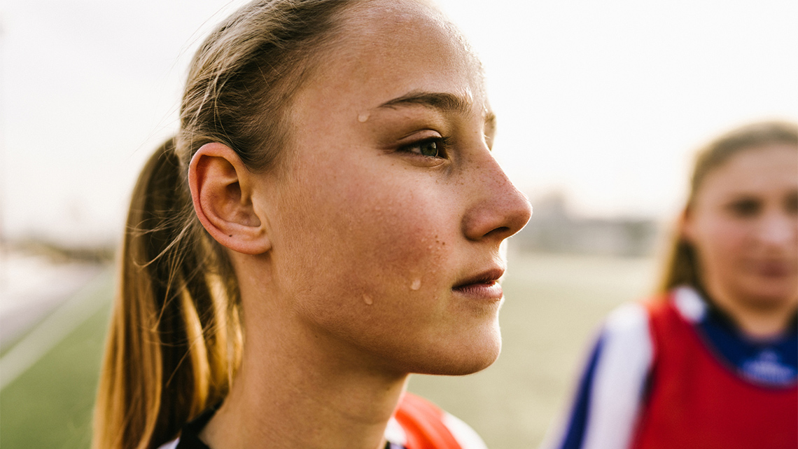 An athlete looks off into the distance, many beads of sweat are on her face.