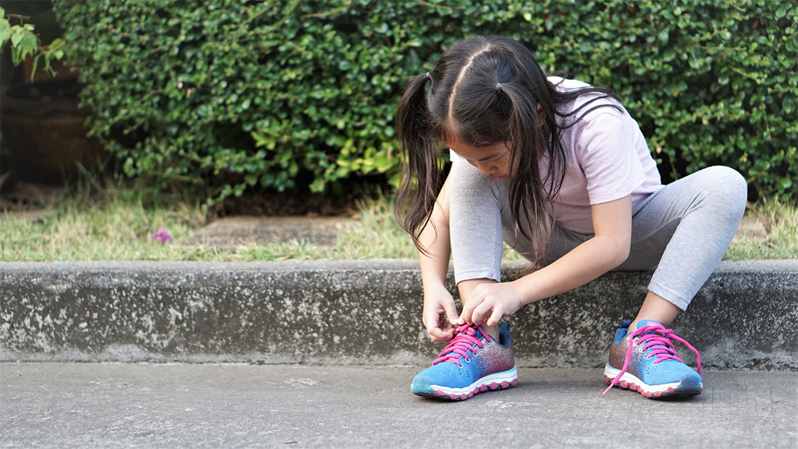 A child is tying their laces on a pair of running shoes. 