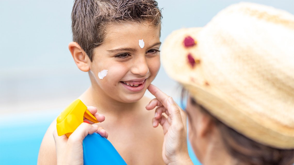 An adult puts sunscreen on a child's face.