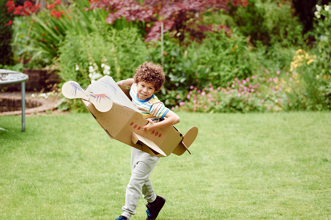 A child wears a set of large homemade cardboard airplane wings and runs outside.