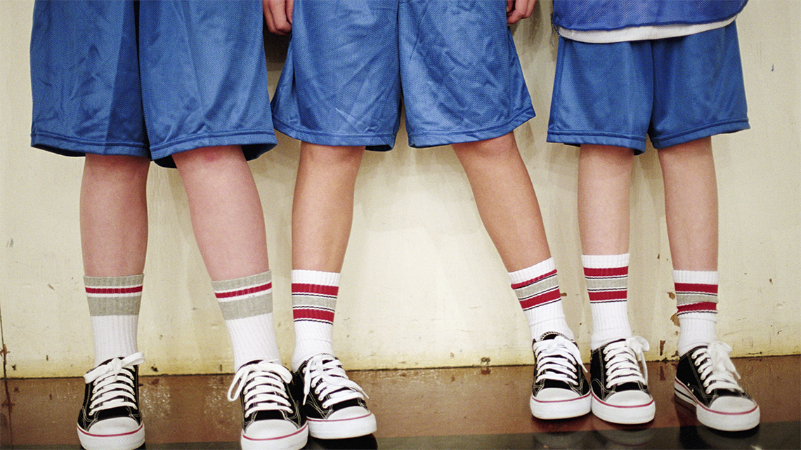 Three students are shown from the waist down. They each wear shorts, athletic socks and running shoes with shoelaces tied.
