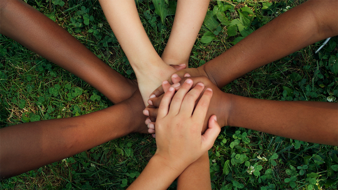 Four children are in a huddle and have placed their hands in the centre, one hand on top of the other.