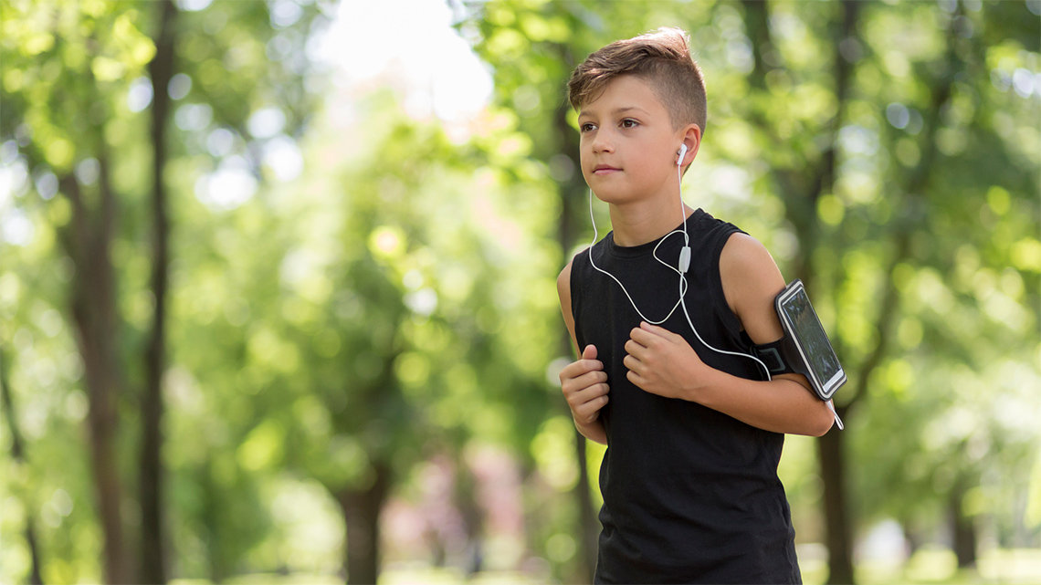 A person is running outside with earbuds in their ear and a cell phone device on their arm. 