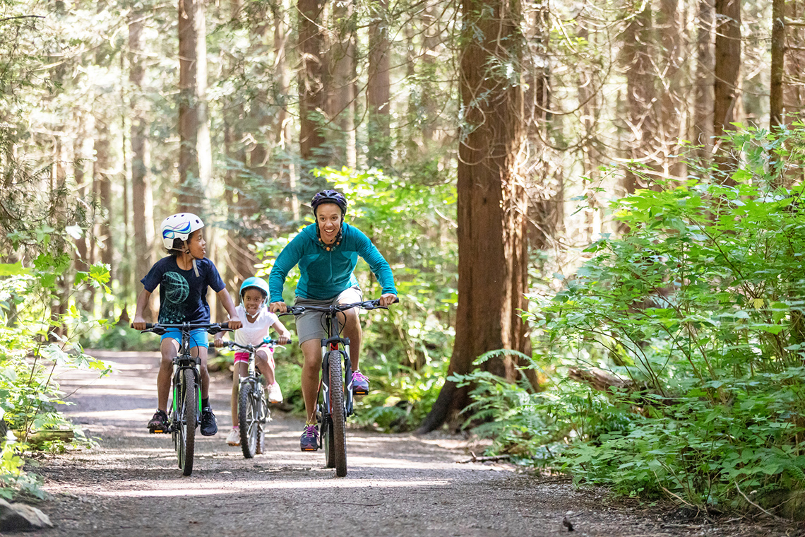 An adult and two children are all wearing helmets as they ride their bike on an outdoor trail.