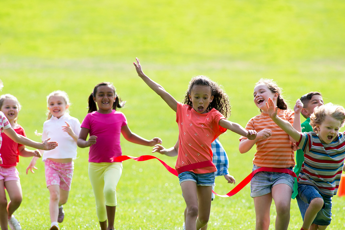 A group of children run towards a finish line. Students who have arrived at the finish line ribbon are excited and happy.