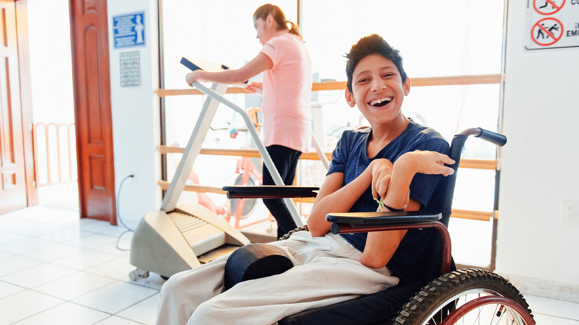 A child in wheelchair is stretching their arms and hands and smiling.