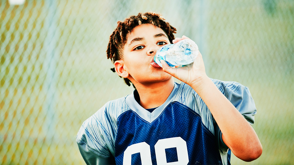 A child in a football jersey is drinking a bottle of water