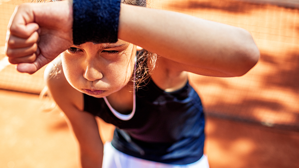 A sweating child exhales and wipes sweat with an wrist sweat band.