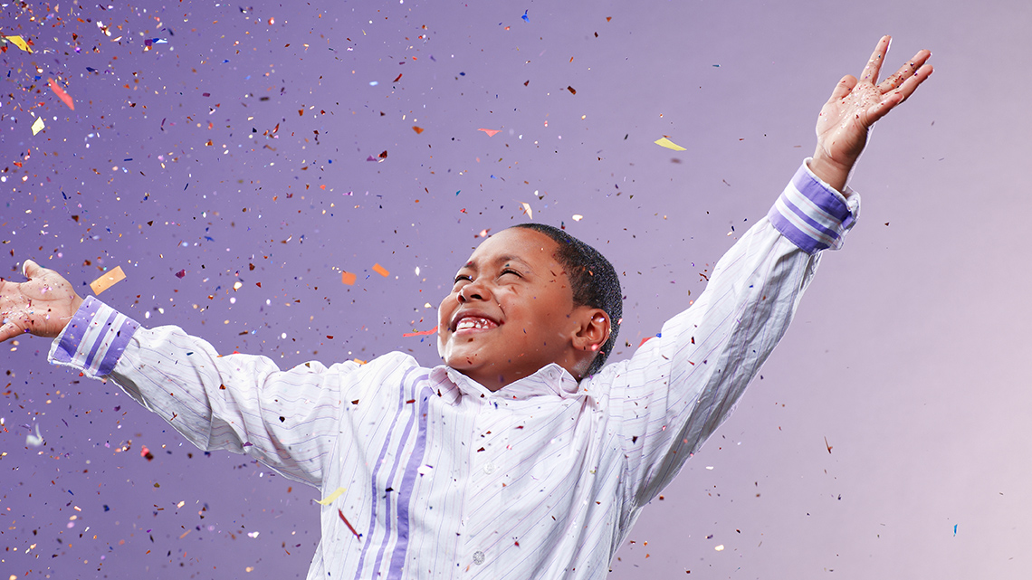 A child with raised hands and confetti all around.