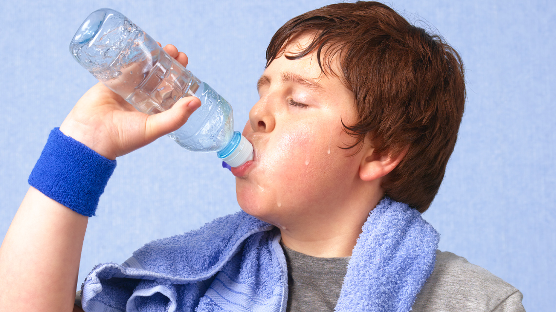 A child sweating and drinking water with a towel around their neck