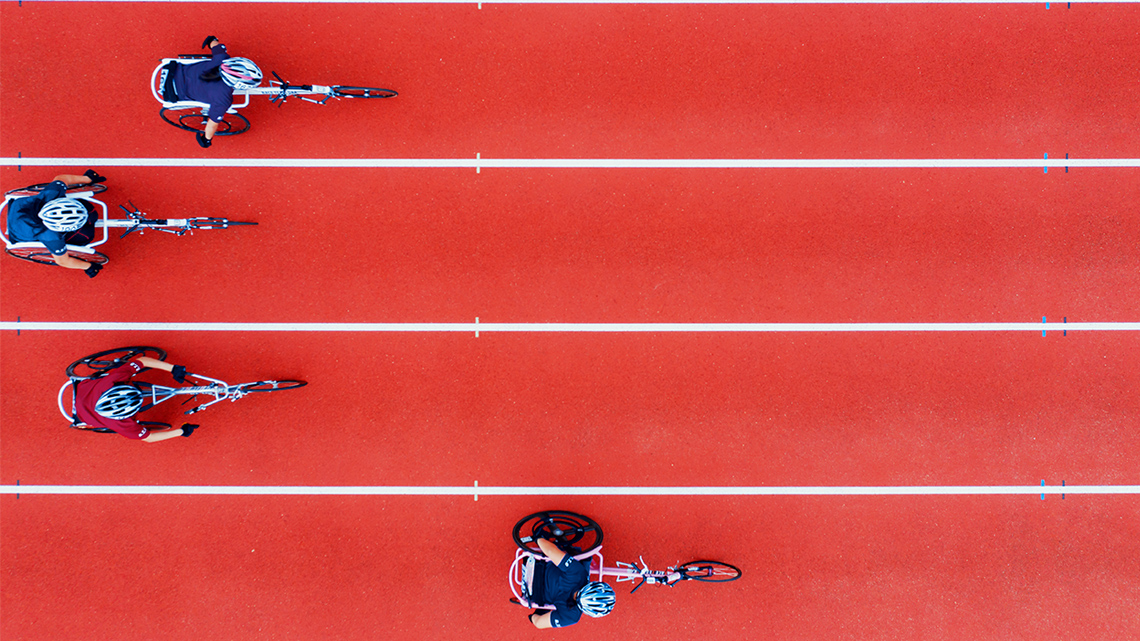 Four people in wheelchairs racing in a track field, photographed from above
