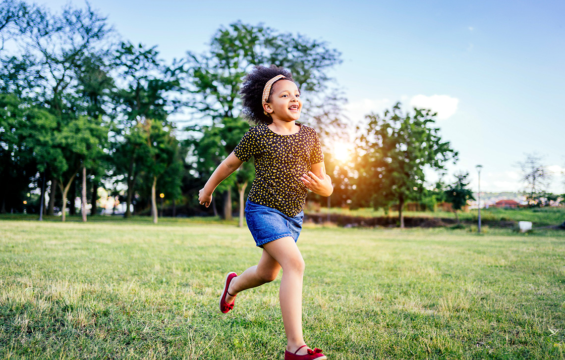 A child running outdoors on a sunny day looking happy.