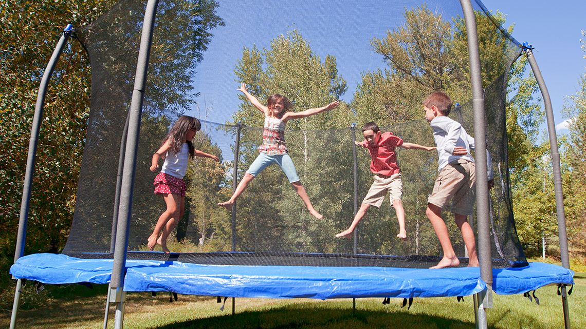 4 children jumping on a trampoline, 2 children are in mid-air with stretched legs and arms.