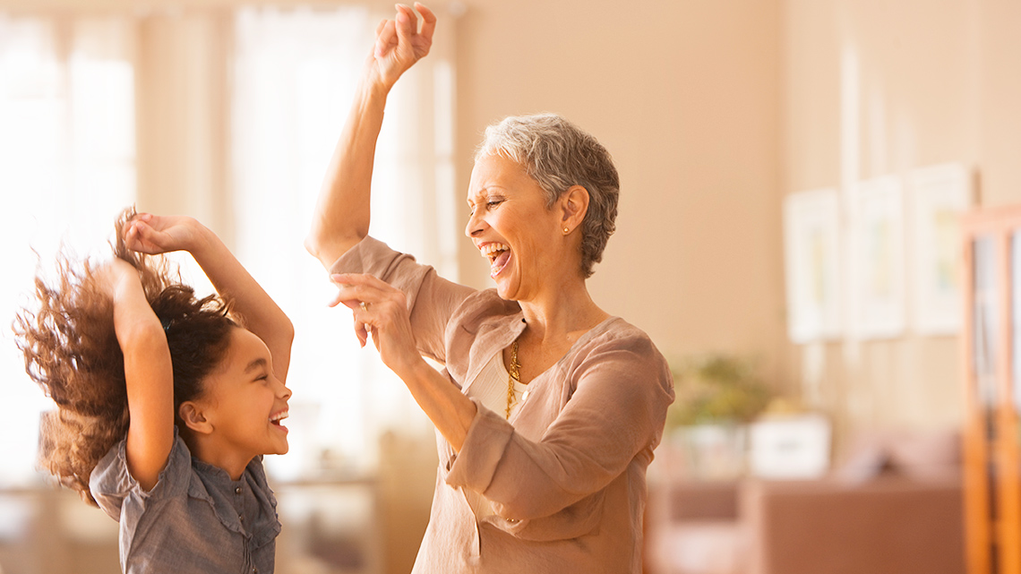 A child and an adult laughing and dancing, hands up in the air.
