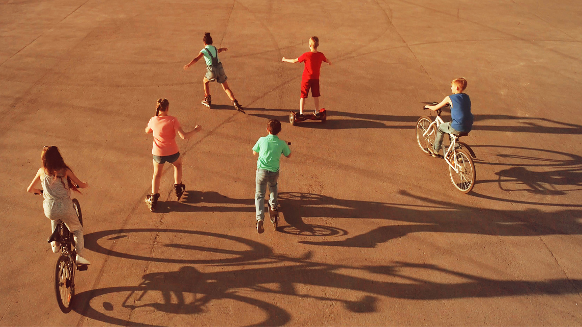 Children rollerblading and cycling in an open space outdoors.