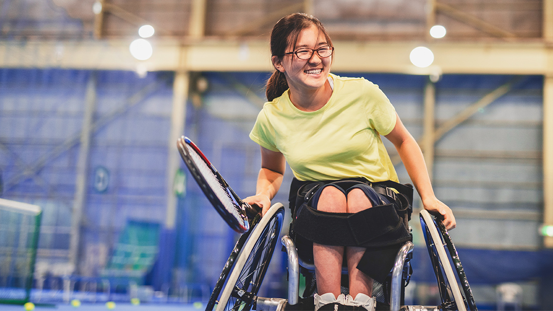 A youth playing wheelchair tennis and smiling.