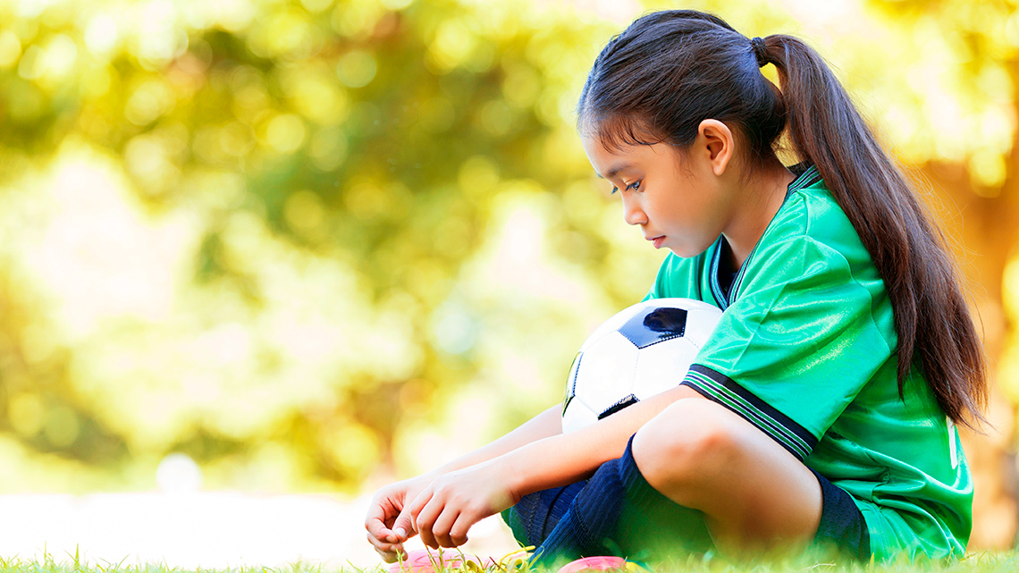 A child sitting on the grass holding a soccer ball.