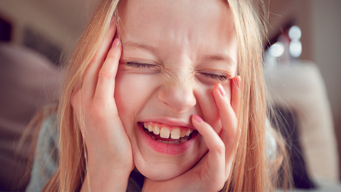 Child is smiling with closed eyes and hands on cheeks.