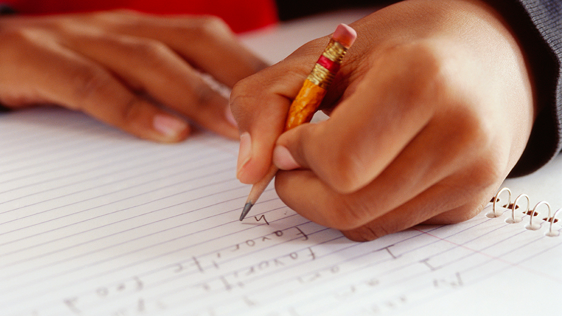 A hand holding a small pencil and writing in a notebook. 