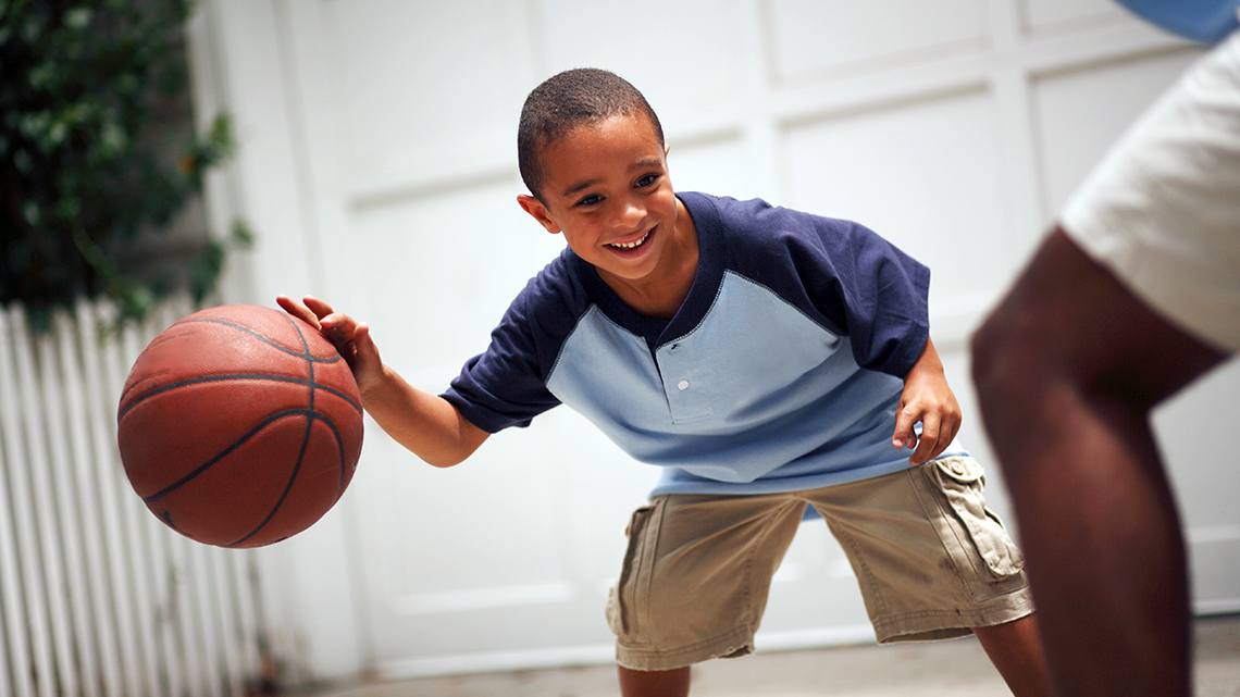 A smiling child is playing basketball with an adult. 