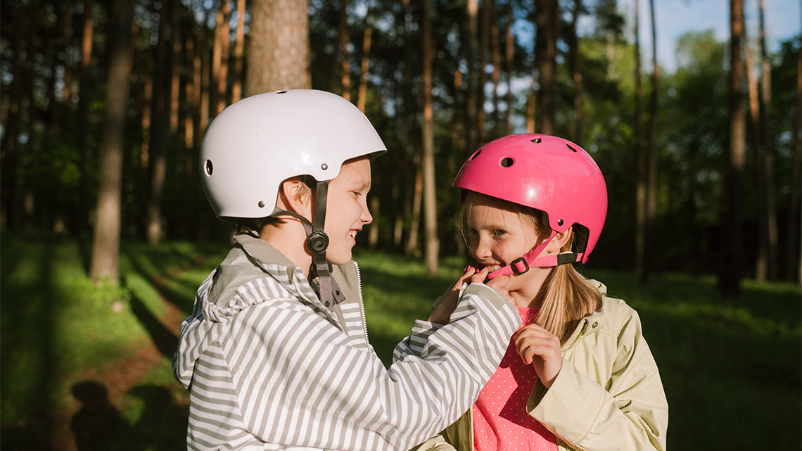 Two children help each fasten their bicycle helmets.