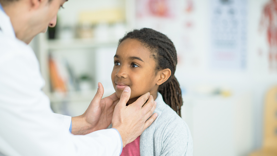 A medical professional checks a child's heart rate by placing their hands on the child's neck.
