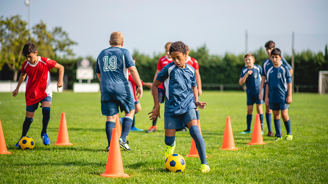 An athlete dribbling a soccer ball through pylons to warm up.