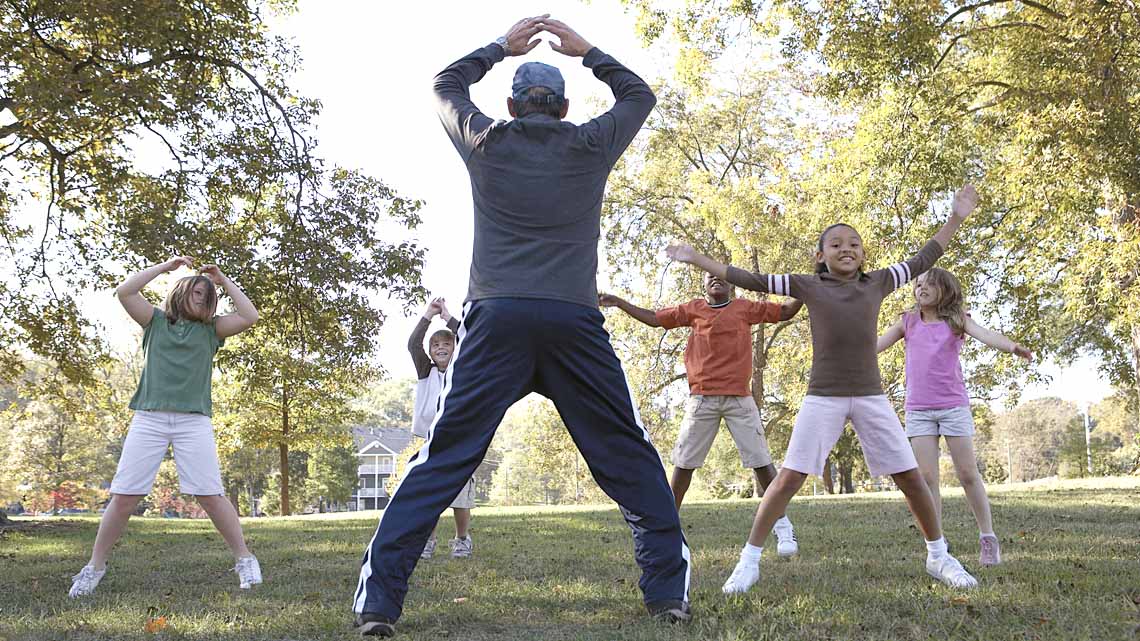 A group of children doing jumping jacks in an outdoor space.