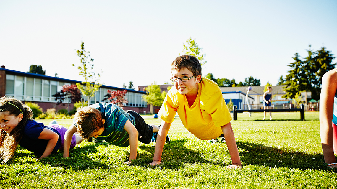 A group of children doing push ups in an outdoor space.