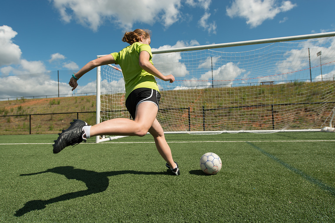 A soccer player kicking a ball into the net.