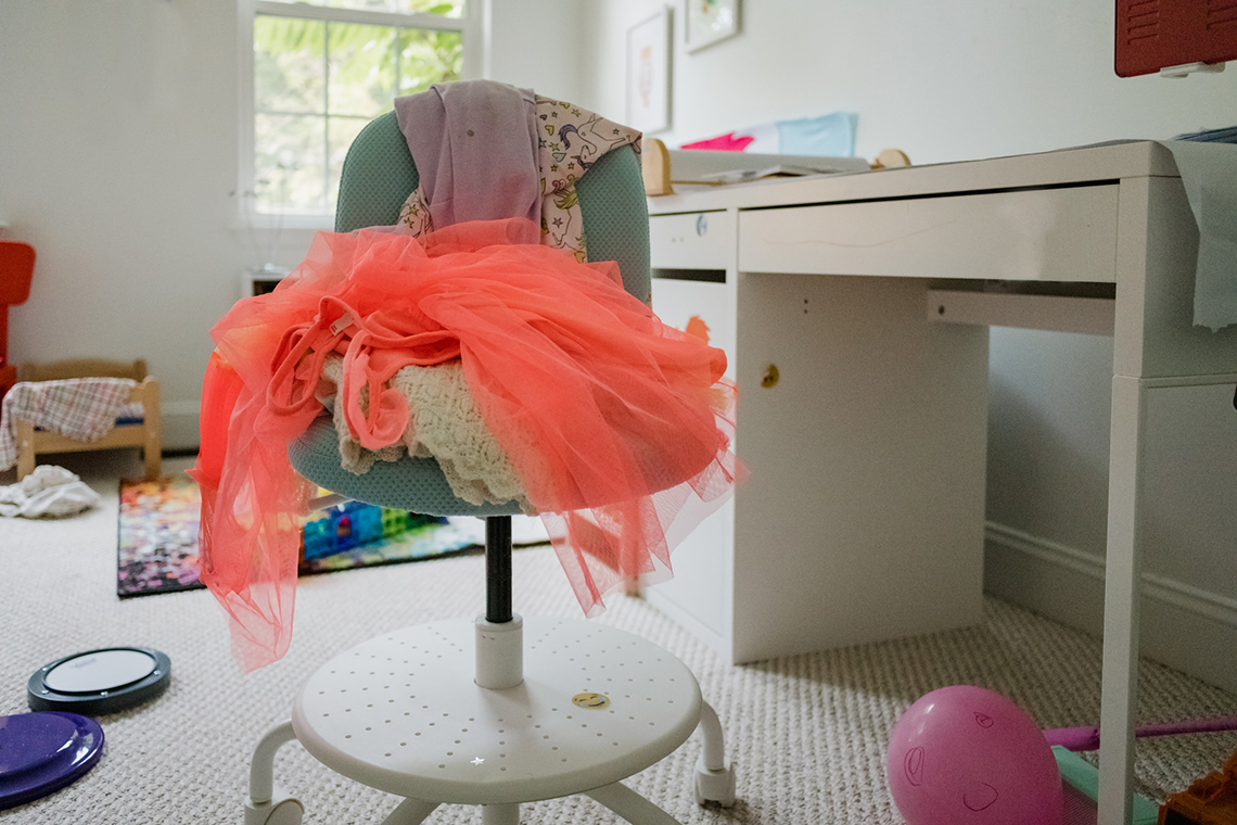 A messy room with stuff everywhere. There is a chair with clothes piled on top of it.