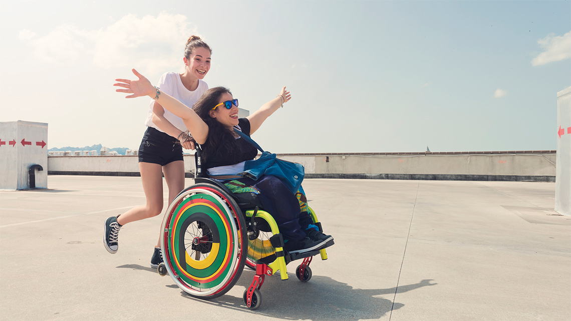 A person pushing their friend in a wheelchair outside. 